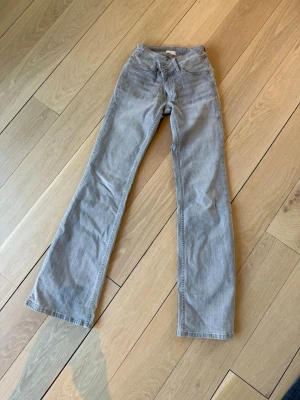 Grå bootcut jeans low waist - Säljer ett par gråa bootcut jeans med låg midja. Jeansen har klassiska fickor fram och bak och är tillverkade av 89% bomull, 9% polyester och 2% elastan för en bekväm passform. Perfekt för dig som gillar en avslappnad och trendig stil.