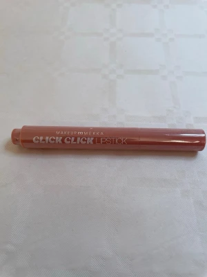 Makeup Mekka Click Click Lipstick nude - Säljer ett Click Click Lipstick från Makeup Mekka i en snygg nude-rosa nyans. Läppstiftet har en smal, rundad form och kommer i en plastförpackning med tryck i vitt. Perfekt för dig som gillar naturliga läppar med en hint av färg.