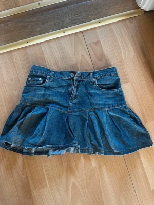 Blå jeanskjol med volang - Snygg blå jeanskjol med volangkant och klassiska fickor fram och bak. Kjolen har en kort modell och stängs med knapp och dragkedja. Den är i storlek xs men skulle säga att den mer är som en S. Jag har sytt in den lite men den är ändå lite förstor för mig.