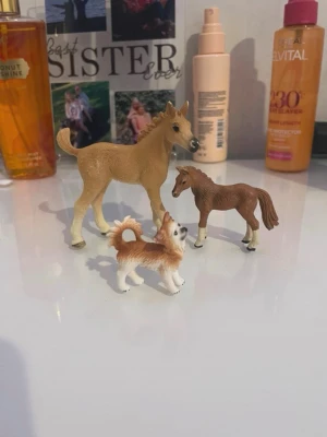 Små djurfigurer häst och hund - Tre realistiska djurfigurer i plast, två hästar i beige och brun samt en hund i vitt och brunt. Perfekta för samling eller lek. Figurerna har fina detaljer och står stadigt på egna ben. Den större jästen och hunden är i Schleich och den lilla bruna är i plast.