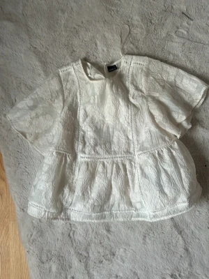 Vit spetsblus från Gina Tricot - Söt vit blus från Gina Tricot i storlek XS. Blusen har korta ärmar, broderade spetsdetaljer och en luftig, lätt utsvängd passform. Perfekt för en romantisk look och passar till både jeans och kjol.