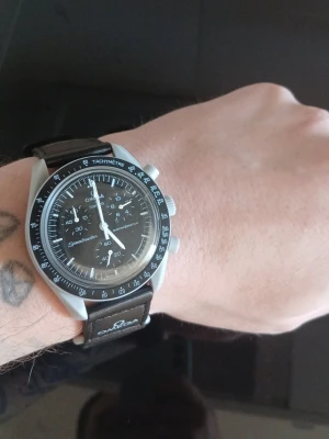 Omega Speedmaster svart klocka - Snygg Omega Speedmaster med svart urtavla och svart textilarmband. Klockan har kronograf, tachymeter och tydliga vita visare och index. Klassisk rund boett i silverfärgad metall och Omega-logga på armbandet. Perfekt för dig som gillar stilrena accessoarer. Köpt på vinted och fick inte med någon kartong. Nypris: 3500kr.