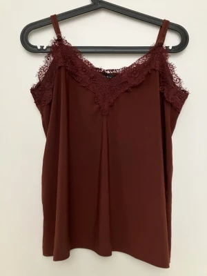 Vinröd linnetopp med spets från Amisu - Supersnygg vinröd linnetopp från Amisu med tunna axelband och v-ringning dekorerad med spets. Perfekt att styla lager på lager eller som den är. Mjuk och lätt i materialet, ger en chic vibe till din outfit.