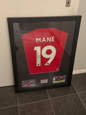 Inramad signerad Mané Liverpool-tröja - Säljer en inramad och signerad Liverpool-tröja med Mané nummer 19. Tröjan är har autograf på siffran. Medföljer äkthetsintyg från Sports Displays samt två foton på Mané i match. Perfekt för fotbollsfans och samlare.