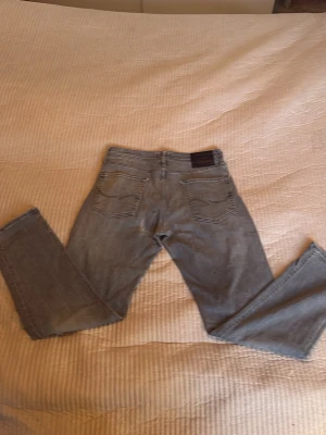 Grå raka jeans från Jack and Jones - Säljer ett par grå jeans från Jack and jones med raka ben och klassisk femficksmodell. Jeansen har normal midja och är tillverkade i ett mjukt denimtyg. Perfekta för en avslappnad och trendig look.