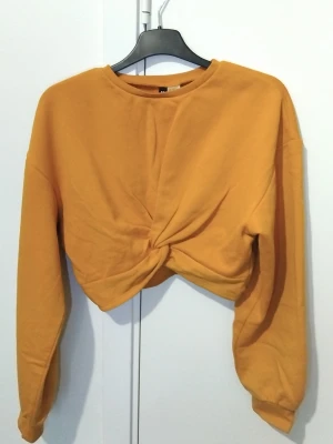 Gul croppad långärmad topp - Snygg gul croppad topp med lång ärm och twistad knutdetalj framtill. Tillverkad i mjuk bomullsmix som känns skön mot huden. Perfekt till höst och vår för en trendig och avslappnad look.