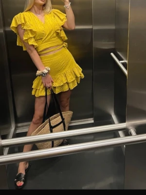 Gul volangkjol från Zara - Säljer en kort gul kjol från Zara med broderade detaljer och volang längst ner. Kjolen har ett luftigt och somrigt material som passar perfekt för varma dagar. Den har en feminin och trendig look med snygga hålmönster och volangkant.