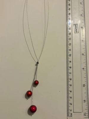 Halsband med röda pärlor - Snyggt halsband med tunn silverfärgad kedja och tre röda pärlor i olika storlekar. Pärlorna sitter i olika höjd för en modern look. Perfekt accessoar för att lyfta din outfit med lite färg. Nickelfitt