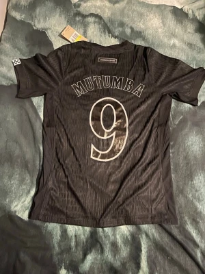 Martin Mutumba tröja - Snygg svart fotbollströja från Nike med namnet Mutumba och nummer 9 på ryggen. Tröjan är tillverkad i lätt och ventilerande Dri-Fit ADV-material som passar perfekt för träning eller match. Klassisk passform och diskret mönster i tyget.