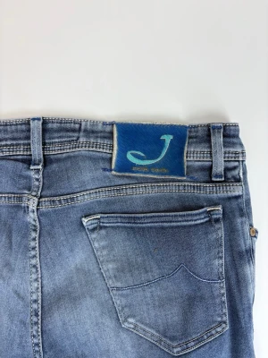 Blå slim fit jeans från Jacob Cohen - Snygga blå slim fit jeans från Jacob Cohen med klassisk femficksdesign och ljus tvätt. Jeansen har en unik blå patch med J-logga bak i midjan och subtila slitningar för en trendig look. Perfekta för dig som gillar stilrena och moderna jeans.