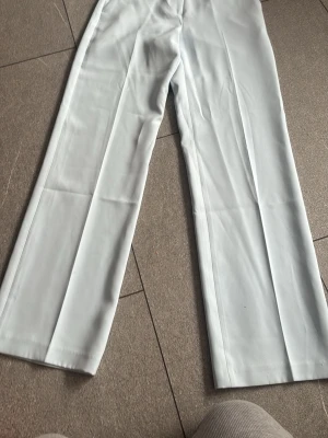 Ljusblå vida kostymbyxor - Snygga ljusblå kostymbyxor med raka, vida ben och pressveck. Byxorna har hällor för skärp och diskreta fickor. Perfekta för en clean och stilren look. Materialet känns slätt och har en lätt glans.