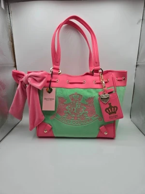 Juicy Couture daydreamer tote - Superfin handväska från Juicy Couture i rosa och grönt med stort emblem framtill. Väskan har dubbla handtag, dekorativ rosett i sammet, hjärtformad nyckelring och detaljer i guld. Materialet är en mix av tyg och sammet med läderdetaljer.