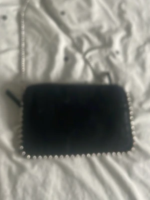 Svart kedjeväska från Zara - Snygg svart handväska från Zara med silverfärgad kedja som axelrem och coola silverdetaljer runt kanterna. Väskan har en rektangulär form och är tillverkad i ett mjukt material. Perfekt för dig som gillar trendiga accessoarer.
