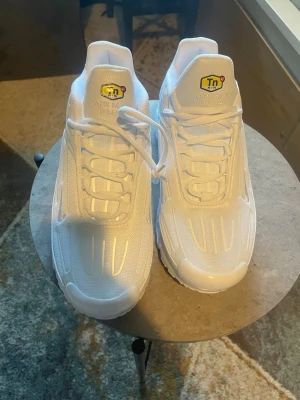 Nike Air Max Plus vita sneakers - Nike Air Max Plus sneakers i helvitt med Tn-logga på plösen. Skorna har en sportig siluett, synlig Air-dämpning i sulan och detaljer i mesh och syntet. Klassisk snörning och robust yttersula för extra komfort. Perfekta för dig som gillar stilrena och trendiga sneakers.