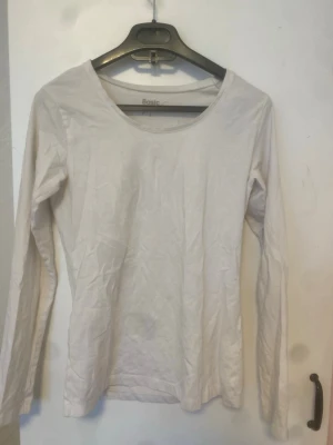 Vit långärmad topp Basic - En enkel vit långärmad topp från Basic med rund halsringning. Tillverkad i mjuk bomull, perfekt att styla lager på lager eller bära som den är. Passar till det mesta och är ett måste i garderoben.