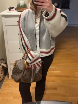 Jaded London Jacka - Snygg grå stickad ziptröja med vita, röda och svarta ränder längs ärmar och kanter. Tröjan har ribbstickade muddar, ståkrage och två fickor framtill. Perfekt för en avslappnad och trendig look.