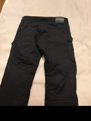 Svarta cargobyxor från Timeless - Svarta cargobyxor från Timeless med flera fickor på sidorna och bak. Byxorna har förstärkta knän och detaljer med sömmar för extra stil. Materialet är slitstarkt och passar perfekt för en aktiv vardag. Klassisk cargomodell med raka ben och cool design. Ny pris 1799