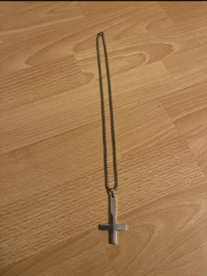 Rostfrittstål halsband med kors - Stilrent halsband med en tunn kedja i silverfärg och ett enkelt kors som hänge. Perfekt accessoar för dig som gillar minimalistisk design. Materialet ser ut att vara metall och kedjan har en klassisk länkstil.