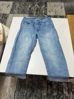 Ljusblå raka jeans - Säljer ett par ljusblå jeans med raka ben och klassisk femficksdesign. Jeansen har en snygg tvätt med lite slitningar och är tillverkade i denim. Perfekta för dig som gillar en avslappnad och tidlös stil.