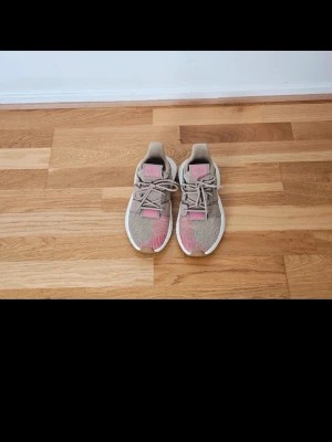 Beige och rosa sneakers från Adidas - Snygga sneakers från Adidas med beige och rosa mesh-överdel, vita sulor och beige detaljer. Skorna har klassiska snörningar och en sportig design som passar perfekt till streetwear. Materialet är mesh och syntet, vilket ger en lätt och luftig känsla.