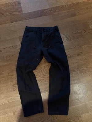 Bruna Carhartt Carpenter pants med raka ben - Säljer ett par bruna Carhartt Carpenter Byxor med raka ben och flera praktiska fickor fram och bak. Byxorna har synliga sömmar och en avslappnad passform, perfekta för en streetwear-look. Materialet är kraftigt bomullstyg.