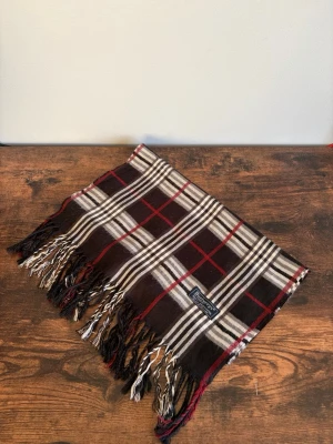 Burberry Halsduk - Vintage Burberrys halsduk i 100% lambswool. Made in England. Klassisk check i mörkare/bruna toner med diskret och tidlös look. Väldigt bra skick med endast mindre tecken på användning. Perfekt för en clean casual/old money stil.