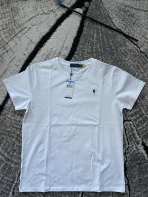 Polo Ralph Lauren - Klassisk vit t-shirt från Polo Ralph Lauren med rund halsringning och broderad logga på bröstet. Tillverkad i mjuk bomull och har en normal passform. Perfekt basplagg med stilren design. Nypris 945kr mitt pris 349kr.