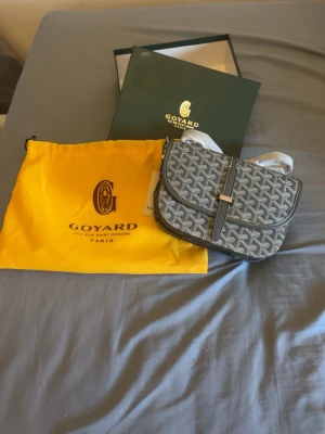 Grå märkes väska med monogram mönster  - Säljer denna gråa märkesväskan med vitt och svart monogram mönster. Helt oanvänd bara tagen ut ur kartogngen, kommer med orgina kartong och påse till axelväskan. Perfekt för dig som vill ha en stilig och lyxig märkes axelväska inför sommarn!