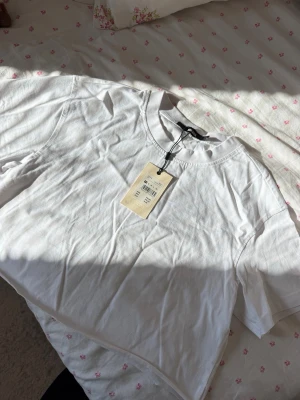 Vit croppad t-shirt från Bik Bok - Säljer en enkel och fräsch vit t-shirt från Bik Bok. Modellen är croppad med rund halsringning och korta ärmar. Perfekt till jeans eller kjol för en clean och avslappnad look. Tillverkad i mjuk bomull för skön känsla.