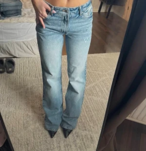 Ljusblå raka jeans från H&M - Säljer ett par klassiska ljusblå jeans från H&M med utsvängd passform och normal midja. dragkedja och knapp framtill samt subtila slitningar för en avslappnad look. Perfekta till sneakers, klackar eller boots.