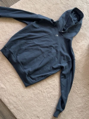 Mörkblå Gymshark hoodie med tryck - Snygg mörkblå hoodie från Gymshark i XXS med stor vit grafisk print på ryggen och liten logga på bröstet. Klassisk känguruficka framtill och huva. perfekt för chill eller gymmet. Använd en gång. 