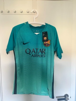 FC Barcelona fotbollströja - Säljer en FC Barcelona röja från Nike i turkos med tunna horisontella ränder. Tröjan har Neymar och nummer 11 på ryggen, samt Qatar Airways och klubbmärke framtill. Lätt och luftig modell perfekt för fotbollsträning eller match. lappen sitter kvar och pris går o diskutera