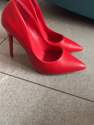 Röda pumps från Sixth Sens - Snygga röda pumps med spetsig tå och hög klack från Sixth Sens. Skorna är i slätt konstläder och har en klassisk siluett som ger en riktigt trendig look. Perfekta för dig som vill sticka ut med färg och stil.
