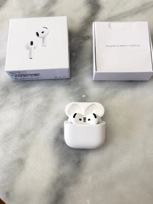 Airpods 4 - Säljer ett par vita Apple AirPods Pro med trådlöst laddningsetui. Hörlurarna har en stilren och kompakt design i blank plast och levereras med originalförpackning. Perfekta för dig som vill ha grymt ljud och brusreducering i vardagen.
