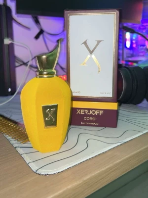 Xerjoff Coro Eau de Parfum 100ml - Lyxig parfym från Xerjoff, Coro Eau de Parfum, i en snygg gul flaska med guldfärgad metallkork och detaljer. Flaskan har en unik form och exklusiv känsla, perfekt för dig som gillar att sticka ut med din doft.