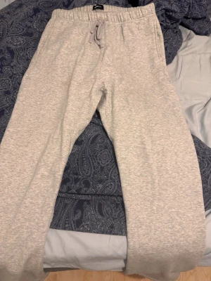 Ljusgrå mjukisbyxor loosefit från Fashionnova - Ljusgrå mjukisbyxor. Med resår och dragsko i midjan. Byxorna är tillverkade i mjukt fleecematerial och har raka ben. Perfekta för chill dagar hemma eller när du vill vara extra bekväm.