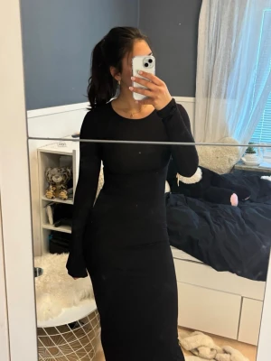 Svart  klänning Gina Tricot - En stilren svart långklänning från Gina Tricot med lång ärm och rund halsringning. Klänningen har en figurnära passform och är tillverkad i ett mjukt och stretchigt material som sitter snyggt på kroppen.