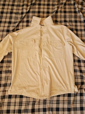 Beige skjorta med bröstfickor - Stilren beige skjorta med två stora bröstfickor och klassisk krage. Skjortan har långa ärmar och knäppning framtill. Perfekt för en avslappnad men ändå snygg look.