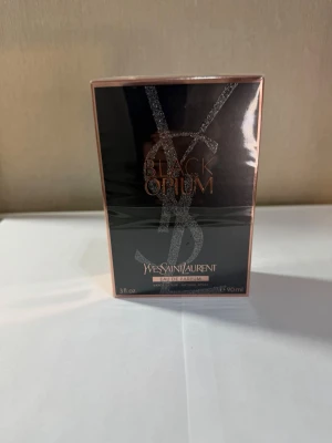 Yves Saint Laurent Black Opium EdP 90ml - Black Opium Eau de Parfum från Yves Saint Laurent i en lyxig svart och roséguldig förpackning. Doften är intensiv och modern, perfekt för dig som gillar en djärv och sensuell parfym. Flaskan rymmer 90 ml och har en snygg design med glittriga detaljer.
