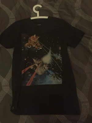 Svart t-shirt med rymdkatter - Cool svart t-shirt med tryck av katter i rymden som skjuter laserstrålar från ögonen. Perfekt för dig som gillar unika och roliga motiv. Klassisk passform och rund halsringning.