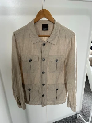Beige overshirt från Oscar Jacobson - Stilren beige overshirt från Oscar Jacobson i linne. Aldrig använd men behöver strykas. Storlek S. Köpt för 2500kr.