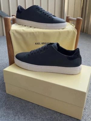 Svarta sneakers från Axel Arigato - Stilrena svarta sneakers från Axel Arigato med minimalistisk design. Skorna har ovandel i slätt läder, svarta skosnören och vit gummisula. Perfekta för dig som gillar en clean och modern look.