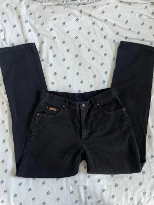 Svarta straight fit jeans från wrangler  - Snygga svarta jeans från wrangler Texas med klassisk rak passform. Jeansen har fem fickor, bälteshällor och wrangler-logga på bakfickan. Tillverkade i bomull med en stilren look som passar till det mesta. Perfekta för dig som gillar en tidlös och enkel stil. W34 L34. 