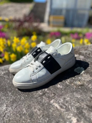 Valentino Opens strlk 43 - Snygga vita sneakers med bred svart läderdetalj över snörningen och vita skosnören. Skorna har en klassisk låg profil och rundad tå. Perfekta för dig som gillar stilrena och moderna sneakers.