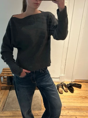 Mörkgrå stickad tröja med bred krage - Säljer en mörkgrå stickad tröja med bred ribbad krage och muddar. Tröjan har en avslappnad passform. Perfekt för lager-på-lager och enkel att styla till jeans eller kjol.