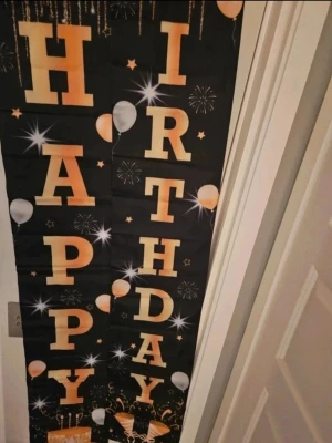 Svart och guld Happy Birthday-banner - Snygg födelsedagsbanner i svart med stora guldiga bokstäver som stavar 'Happy Birthday'. Dekorerad med ballonger, stjärnor och fyrverkerier. Perfekt som dekoration till kalas eller fest. Tillverkad i tyg eller plastliknande material och hängs enkelt upp på väggen eller dörren.
