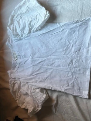 Vit topp med puffärmar från H&M - Säljer en vit topp från H&M med trendiga puffärmar och rund halsringning. Tillverkad i mjukt bomullstyg som känns skönt mot huden. Perfekt för dig som vill ha en enkel men ändå statement topp till din outfit.