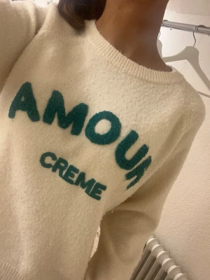 Saint tropez vit cozy amour tröja - ❣️nypris runt 6 €, säljer BILLIGT❣️ Mysig stickad tröja i cremevitt med grönt texttryck 'AMOUR CREME' framtill, köpt i saint tropez. Tröjan har rund halsringning och långa ärmar. Perfekt för dig som gillar en trendig och avslappnad stil.