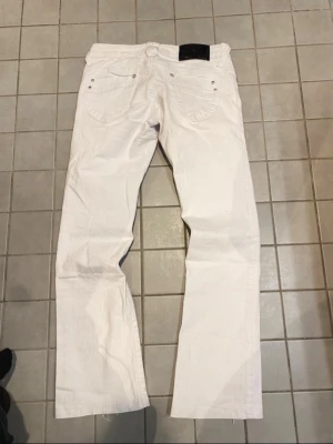 Vita jeans från madonna  - Säljer ett par vita jeans från Madonna med raka ben och klassisk femficksdesign. Jeansen har en svart läderpatch med M.-logga bak i midjan och silverfärgade nitar vid fickorna. Materialet är denim i bomull och passformen är bra. Jag köpte dem på vinted men var mindre än jag trodde. Priset kan diskuteras 💕