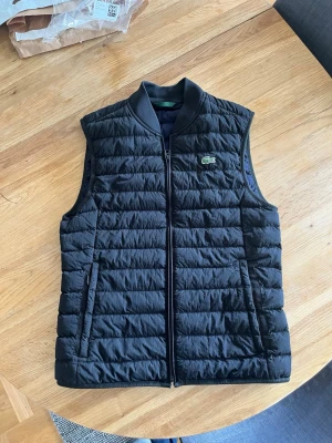 Lacoste väst - Snygg svart dunväst från Lacoste med klassisk quiltad design och dragkedja framtill. Riktigt fet. Sprillans ny, perfekt för vår kvällar. 